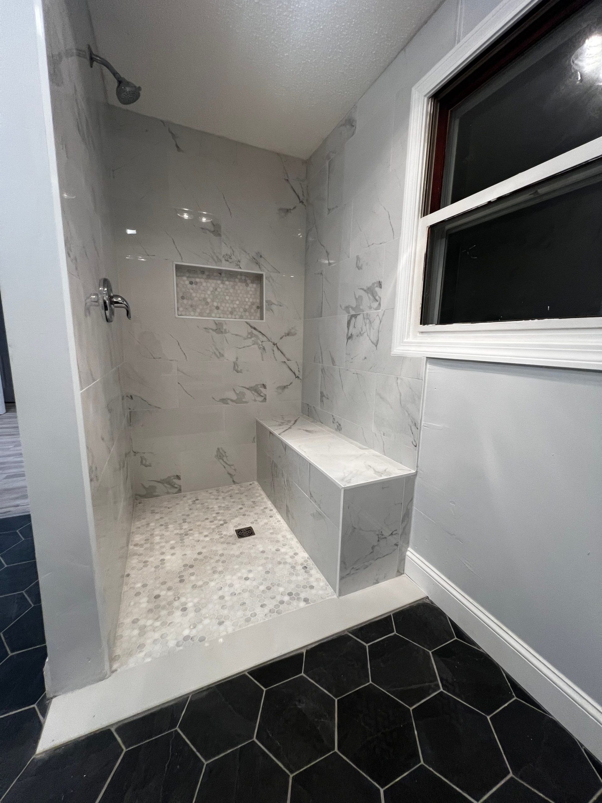 shower stall after remodeling, image shows new mosaic tile floor, large format tile walls, custom shower bench, and newly tiled bathroom floor outside the shower
