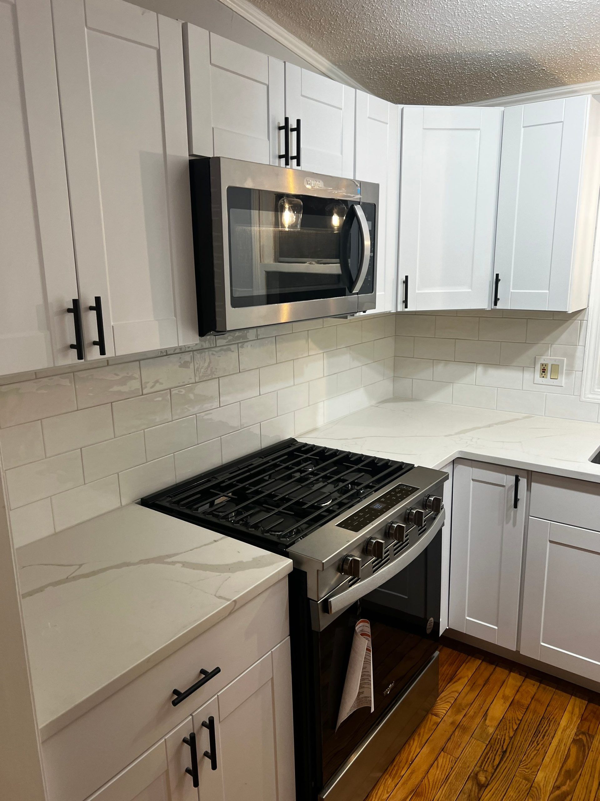 kitchen post remodeling, image shows subway tile backsplash, new shaker style cabinets, stainless steel stove and microwave